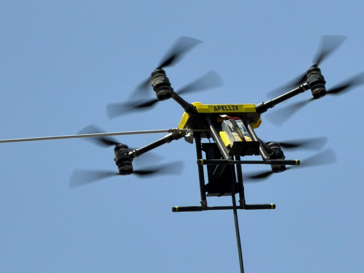 Tethered cleaning drone in flight with a controlled spray nozzle against a blue sky.