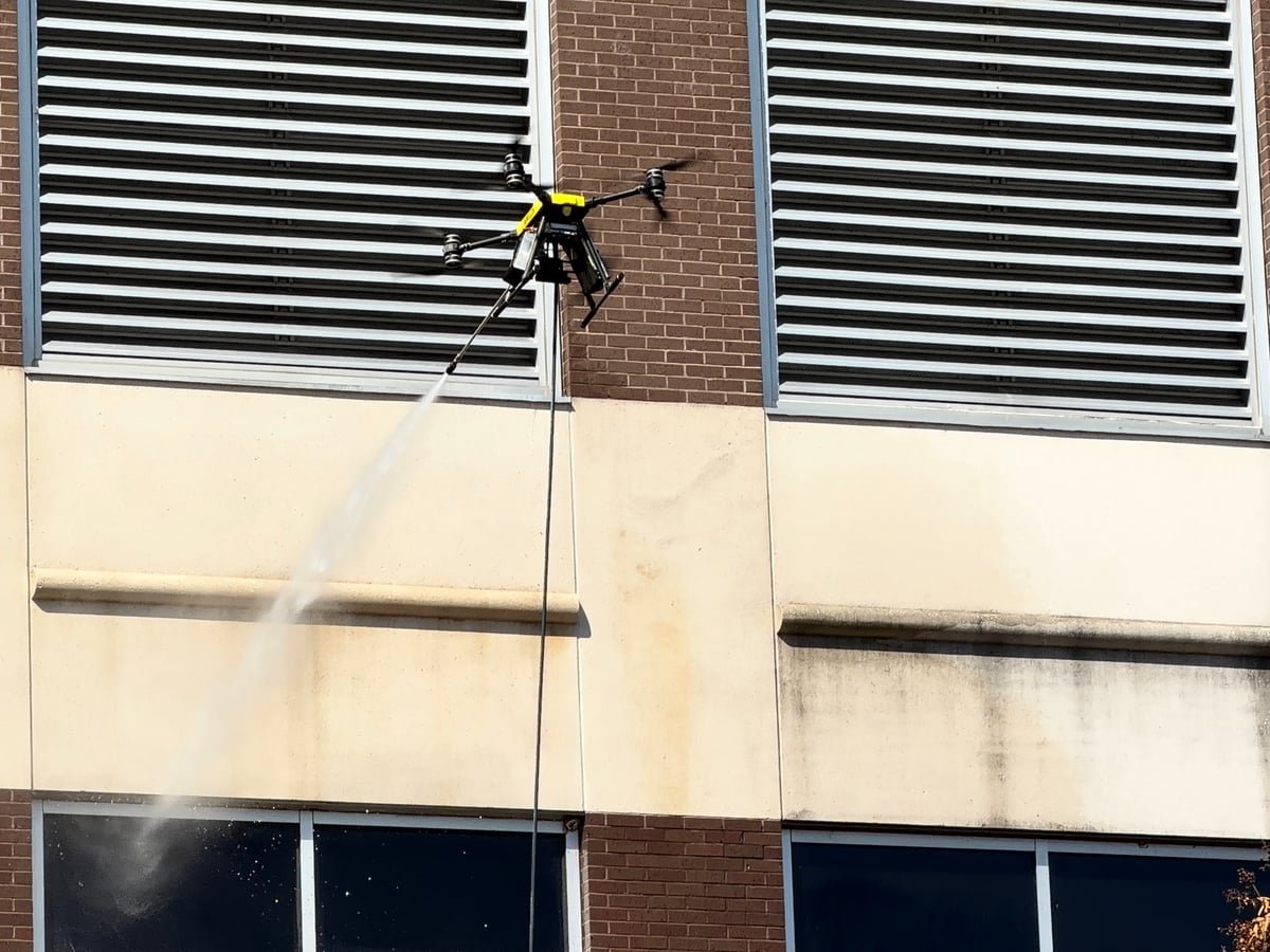 Rotag cleaning drone works beside exterior louvers on a commercial facade.